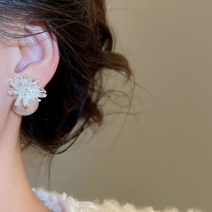 Close-up of silver floral stud earrings with tiny diamonds and round pearl drop on model