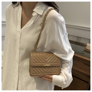 Detail of beige V-quilted faux leather shoulder bag with gold chain strap on a model