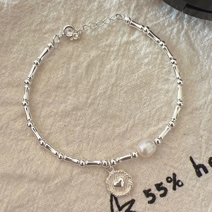 Detail view of silver beaded bracelet with freshwater pearl and heart charm on linen