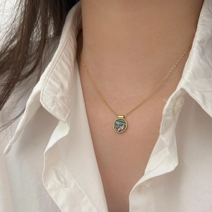 Close-up of gold chain necklace with abalone shell pendant worn on white linen shirt