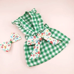 Detail of green plaid pet dress with floral bow accessory on soft pink background