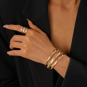 Detailed close-up of a tiered gold metal bangle set and rings with diamond-cut textures