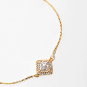 Detail shot of a square gold box chain bracelet featuring a sparkling zircon pendant