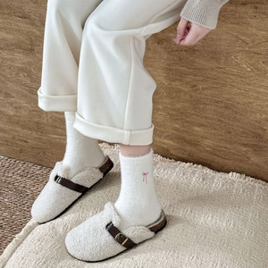Detail showing plush cream slippers with brown leather buckle and pink bow embroidered socks