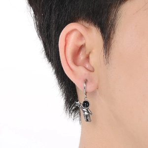 Close-up of silver astronaut dangle earring worn by model on white background