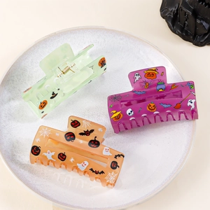 Three Halloween themed square hair claws in transparent green, purple and orange colors