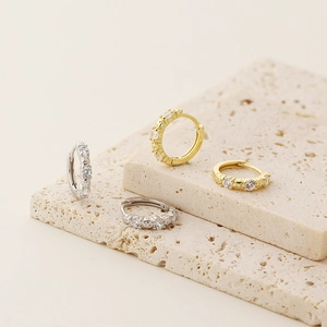 Detail of silver and gold huggie earrings with clear cubic zirconia on stone plates