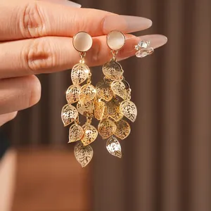 Exquisite gold leaf tassel earrings with cat eye stones shown in a hand-held closeup