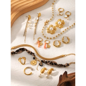 Close-up of gold twist earrings, pearl necklaces and rings on white textured fabric