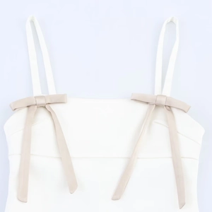 White satin slip dress featuring elegant beige bow accents and minimalist thin straps