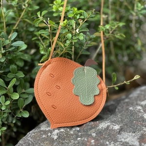 Close-up of orange peach-shaped kid's crossbody bag with litchi grain texture on a rock