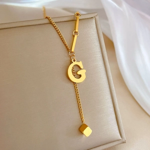 Detail of gold titanium steel necklace featuring G pendant and small cube drop charm