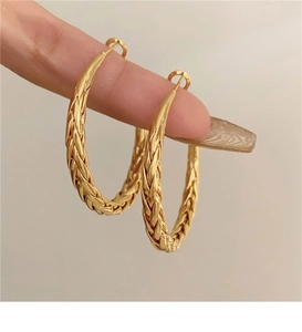 Close-up of gold twist hoop earrings with detailed woven texture on metal surface