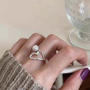 Silver heart shaped open ring with a white pearl accent on a hand with a sweater