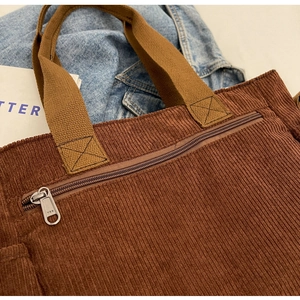 Detailed macro shot of the brown corduroy fabric texture and metal zipper on the tote bag