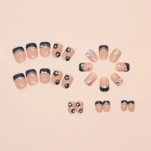 Présentation à plat de faux ongles avec pointes françaises noires, fleurs et strass