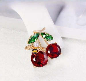 Close-up of red cherry brooch with green enamel leaves and tiny pearl bee detail