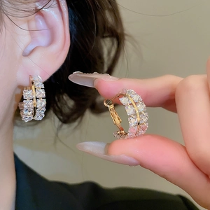 Détail de boucles d'oreilles créoles dorées serties de zircons portées par un modèle