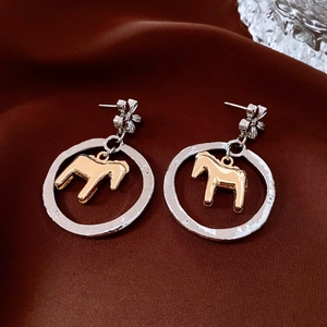 Detail of silver textured hoop earrings featuring a gold horse silhouette on silk fabric