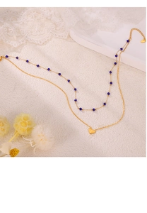 Close-up of double-layer gold necklace with blue beads and heart pendant on white fabric