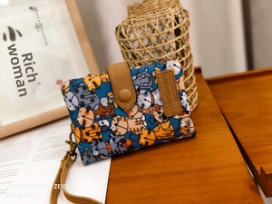 Detail of a bifold cat print wallet with leather closure and brown hand strap on a desk