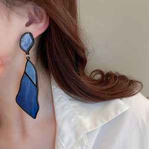 Close-up of blue geometric acrylic drop earrings with fluid texture on model