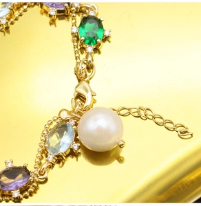 Macro detail of gold bracelet with colorful oval stones and a white pearl pendant
