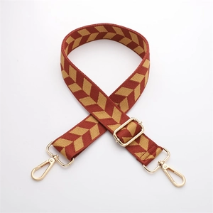 Detail of red woven bag strap with golden chevron pattern and adjustable metal hardware