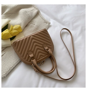 Detail of tan shell bag featuring V-shaped quilting and metal zipper on white bedding