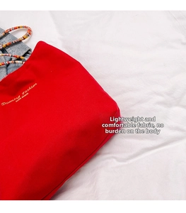 Detalle del bolso tote de lona roja con letras doradas impresas y tela suave y duradera