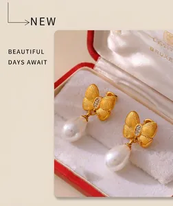 Detailed shot of gold bow earrings with small rhinestones and white teardrop pearl in a red box