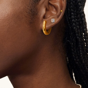 Three-piece set of gold stainless steel hoop earrings and zircon studs on a model's ear