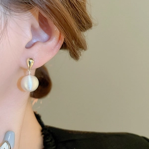 Gros plan d'une boucle d'oreille pendante en perle dorée portée par un mannequin chic