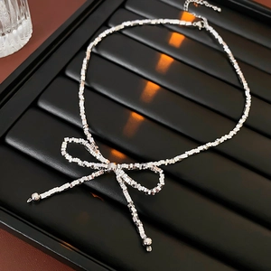 Close-up of silver square link necklace featuring a textured bow pendant and ball charms