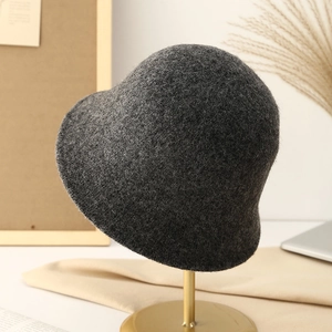 Dark grey knitted bucket hat for women on a gold stand in a minimalist warm setting