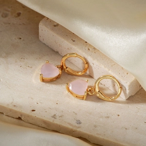 Macro shot of gold heart drop earrings with pink stones on elegant silk fabric