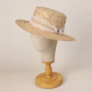 Détail d'un chapeau plat en raphia avec bordure en dentelle blanche et pendentif en métal