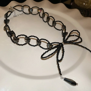 Detail of a black beaded choker with glass butterfly accents and drop pendant on a tray