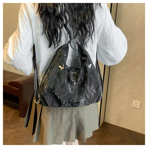 Detail of black pleated leather backpack with silver butterfly clasp on a model's back