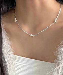 Detail of silver snake chain necklace with mini bow pendants worn on collarbone