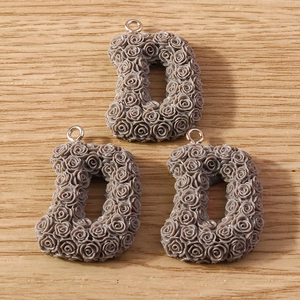Macro shot of three taupe letter D pendants with rose textures and silver hooks on wood