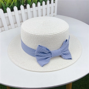 Close-up of white boater straw hat with blue striped ribbon bow on a white table