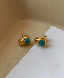 Macro shot of 18k gold plated stud earrings with round turquoise stones on a beige backdrop