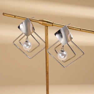 Detail of silver geometric earrings with hanging pearls on a professional display stand