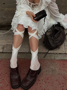 Detail of white lace mesh socks with cross-strap design and ruffled edge on stone pavement