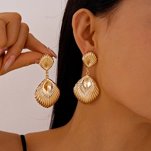 Close-up of golden seashell drop earrings featuring realistic 3D textures on model