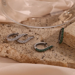 Close-up of wavy silver earrings with green and white zircons on a satin backdrop