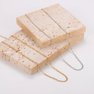 Gold and silver stainless steel link chains displayed on minimalist beige stone texture