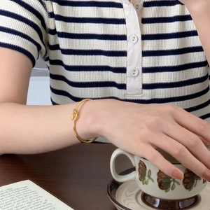 Intertwined gold-tone bangle with sparkling micro-zirconia details worn by model