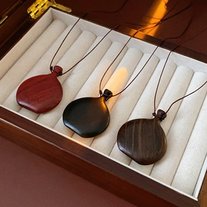 Detailed close-up of three wood wine bag pendant necklaces in red, black, and brown grain